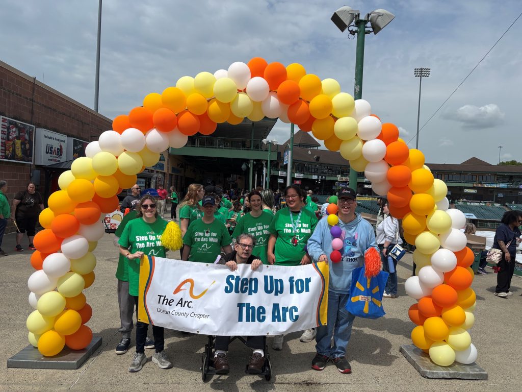 people standing under a balloon arch holding a banner