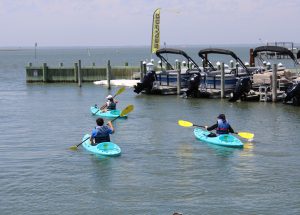 Three people kayaking leaving a marina with boats at the dock