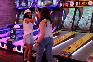 Two women high fiving and playing skee ball