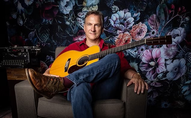man sitting on a couch holding a guitar
