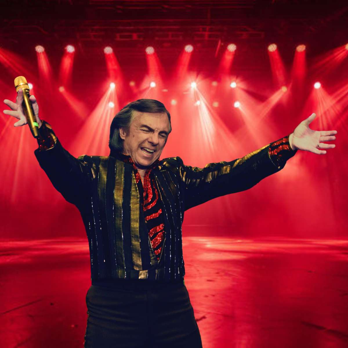 A man holding a microphone on a stage with red lights in the background