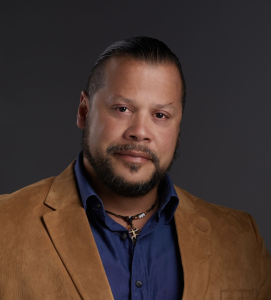 Photo of a man in a brown suit jacket and blue shirt